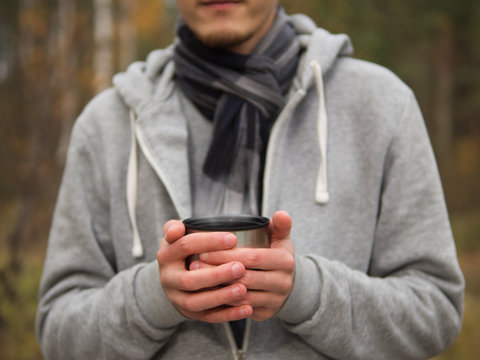 man drinking hot tea from a thermos during a walk through the autumn forest