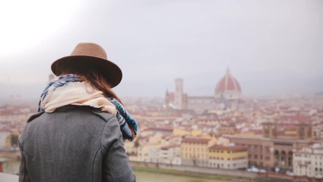Happy tourist girl taking smartphone photo of amazing panoramic view of winter rainy Florence, Italy, walking away.