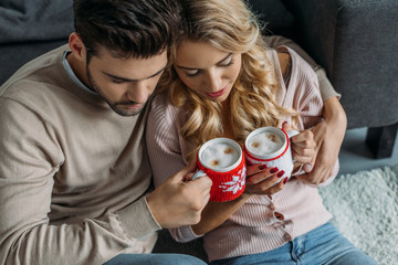 high angle view of couple clinking with cups of cappuccino at home, christmas concept
