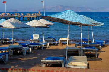 Fototapeta na wymiar Beach with blue sun umbrellas and loungers. The coast resorts of the Aegean Sea of Turkey. Turgutreis , Bodrum.