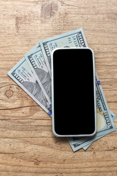 USA currency. Dollars. blank smartphone screen and cash bills on wooden table.