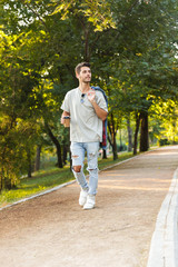 Young man walking in park outdoors holding coffee.