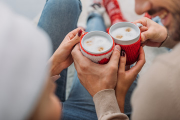 cropped image of couple clicking with cups of cappuccino at home, christmas concept