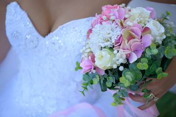 Cropped shot of Caucasian young bride wearing a white sexy, revealing dress and holding a beautiful bridal bouquet of mixed summer flowers and greenery, an essential accessory for a white wedding