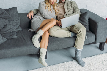 cropped image of couple watching something on laptop on sofa in living room