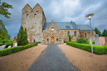 Fototapeta na wymiar Aa church against cloudy sky in Aakirkeby, Denmark. It is the biggest and oldest church on the Bornholm island, constructed from greensand stone, dominates with its twin towers