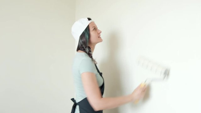 Painting walls with roller. A young woman painting walls in beige in her home with a roller. Close up.