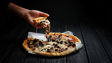 traditional italian pizza on dark black wooden board, piece of pizza in hand,