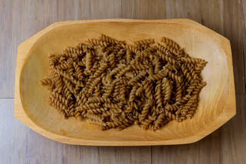 portion of raw whole noodles, wooden bowl, twisted, wooden table top view