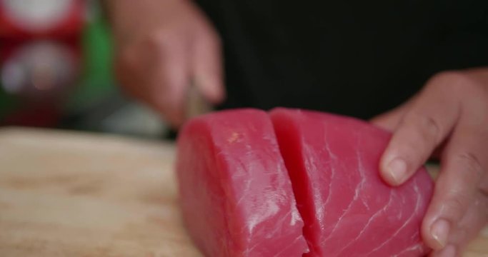 Closeup woman's hands cutting up raw fillet of salmon with sharp knife. Closeup of chef preparing fresh salmon steak on a wooden cutting board - video in slow motion