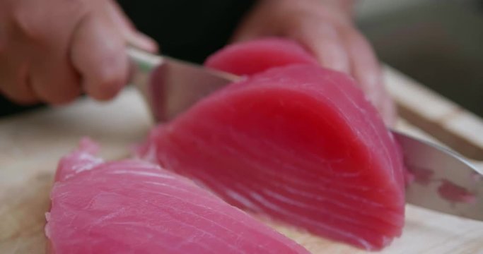 Closeup woman's hands cutting up raw fillet of salmon with sharp knife. Closeup of chef preparing fresh salmon steak on a wooden cutting board - video in slow motion