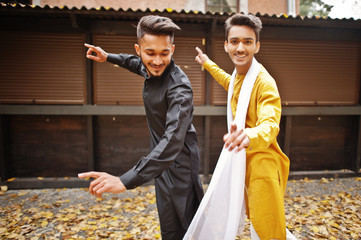 Two indian stylish mans friends in traditional clothes dancing outdoor. Navaratri dance.
