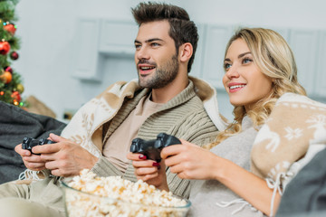 beautiful young couple with popcorn playing video games together on couch at home