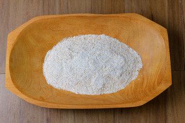 portion of raw whole wheat flour, wooden bowl, wooden table top view