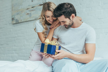 beautiful young woman presenting gift to boyfriend in bed at home