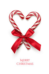 Two red striped candy cane in heart shape with red bow and Merry Christmas text isolated on white background. Vector Christmas design element.