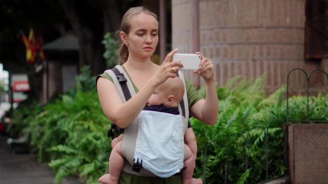 A woman with a baby travels on the island a child sits in a sling.