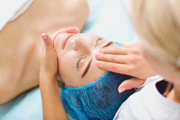 Cosmetologist makes facial massage to a young woman in the spa salon.