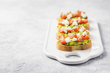 Avocado cherry tomatoes toasts on board. Selective focus, space for text.