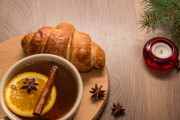 A cup of tea with a croissant on a wooden background with New Year's decor