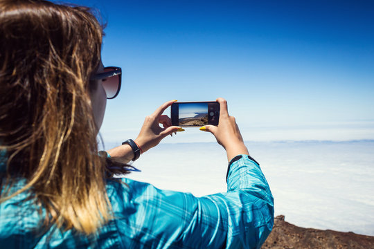 Young woman taking a photo with her phone of amazing mountains landscape on Tenerife, Canary islands, Spain. Travel concept
