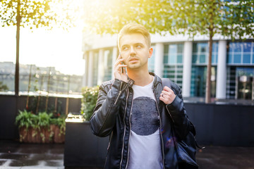Attractive stylish young man in a leather jacket with a mobile phone with a smartphone in his hands...