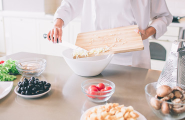 Cut view of woman's hands putting meal into white bowl. She uses knife for that. Girl is cooking.
