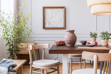 Clay vase on the table in a dining room interior with a plant, chairs and art on a wall
