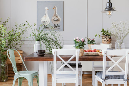 Real photo of plants in a rustical dining room interior with a table, chairs, painting with ducks