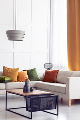 Green, orange and yellow pillows on the white corner sofa in stylish living room, real photo with copy space
