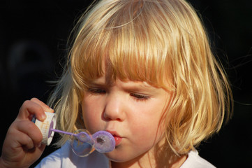 Small blond girl blowing bubbles.