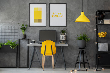 Stylish yellow and grey home office with industrial furniture and urban jungle, real photo with...