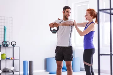  Smiling personal trainer and sportswoman working out with weight at gym © Photographee.eu