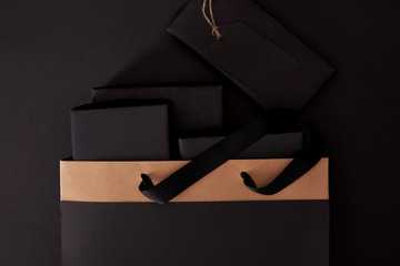 top view of black boxes in shopping bag on black surface, black friday concept
