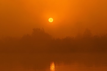 Mglisty wschód słońca nad rzeką w pomarańczowych kolorach.