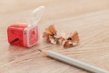 Red pencil sharpener and pencil and pencil shavings on wooden floor.
