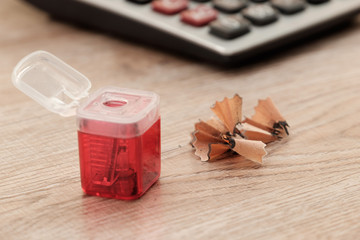 Red pencil sharpener  and pencil shavings and calculator on wooden floor.