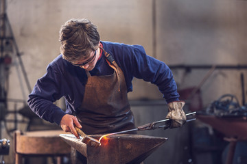 Young blacksmith working with red hot metal - 229388880