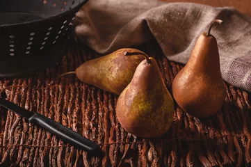 Fotobehang Still life scene of three pears, a paring knife, colander and towel on a woven twig background. © Anne Stephenson