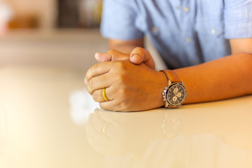 Man's left hand with gold wedding ring on his finger on marble table.