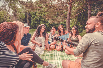 group of young people chilling with beer and guitar music having fun outdoor in summer vacation