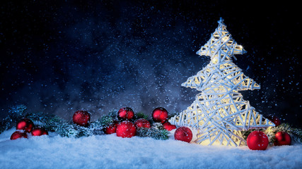 Leuchtender Weihnachtsbaum mit Weihnachtskugeln und Tannenzweig vor dunklem Hinterdrund mit Schnee