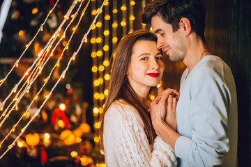 A guy with a girl is celebrating Christmas. A loving couple enjoy each other on New Year's Eve. New Year's love story. Man and woman enjoy the moment and playing with garlands.