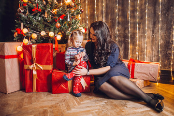 Portrait of beautiful mother and dauther near the Christmas tree. Family woman with little child in a festive New Year's atmosphere. Happy holiday moment.