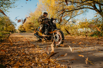 young man on a motorcycle rides through an autumn alley with leaves