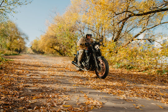 young man on a motorcycle rides through an autumn alley with leaves