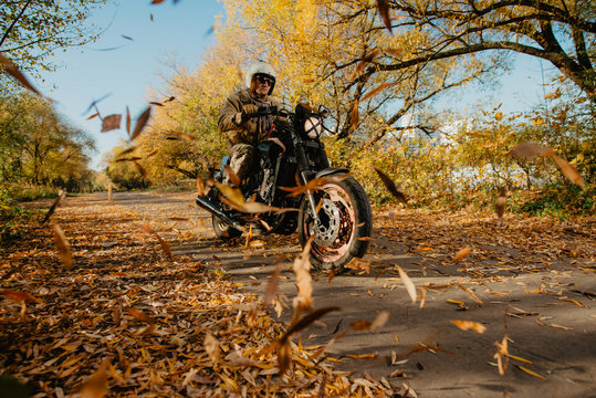 Fototapeta young man on a motorcycle rides through an autumn alley with leaves