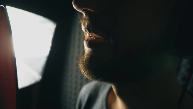 Mouth of male singer singing in sound studio. Unrecognizable man recording new song. Guy with beard sings to microphone. Working of creative musician. Show business concept. Slow motion Close up