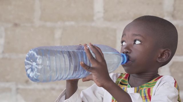 Horizontal shot of a native African child drinking water from a plastic bottle. 4K RAW clip, please modify and edit (color grade, stabilize, etc.) in postproduction.