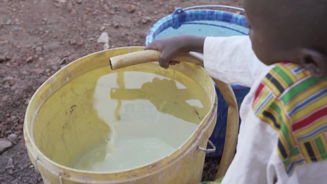 Close-Up footage of an African black child playing outdoors with a water hose. Water scarcity and the lack of fresh water will be a huge problem for the future of Africa. 4K RAW clip, please modify an